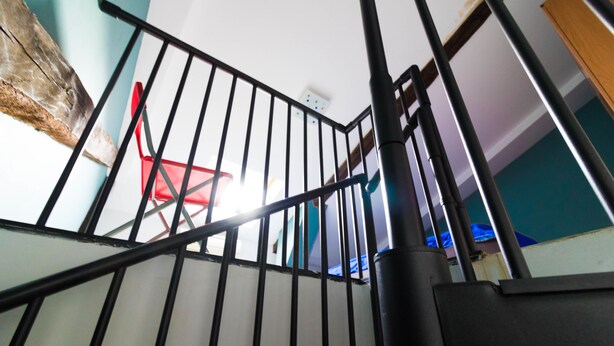 Una escalera con barandillas negras y una silla roja visible al fondo.