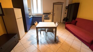 Cocina compacta con mesa, sillas, refrigerador, microondas y sofá rojo.