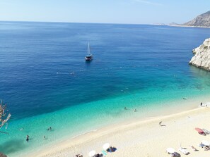 Uma praia com águas turquesa cristalinas, um veleiro e pessoas nadando e tomando sol.