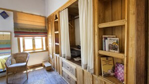 Ein Zimmer mit einem hölzernen Bücherregal, einem Korbstuhl und einem Vorhangfenster.
