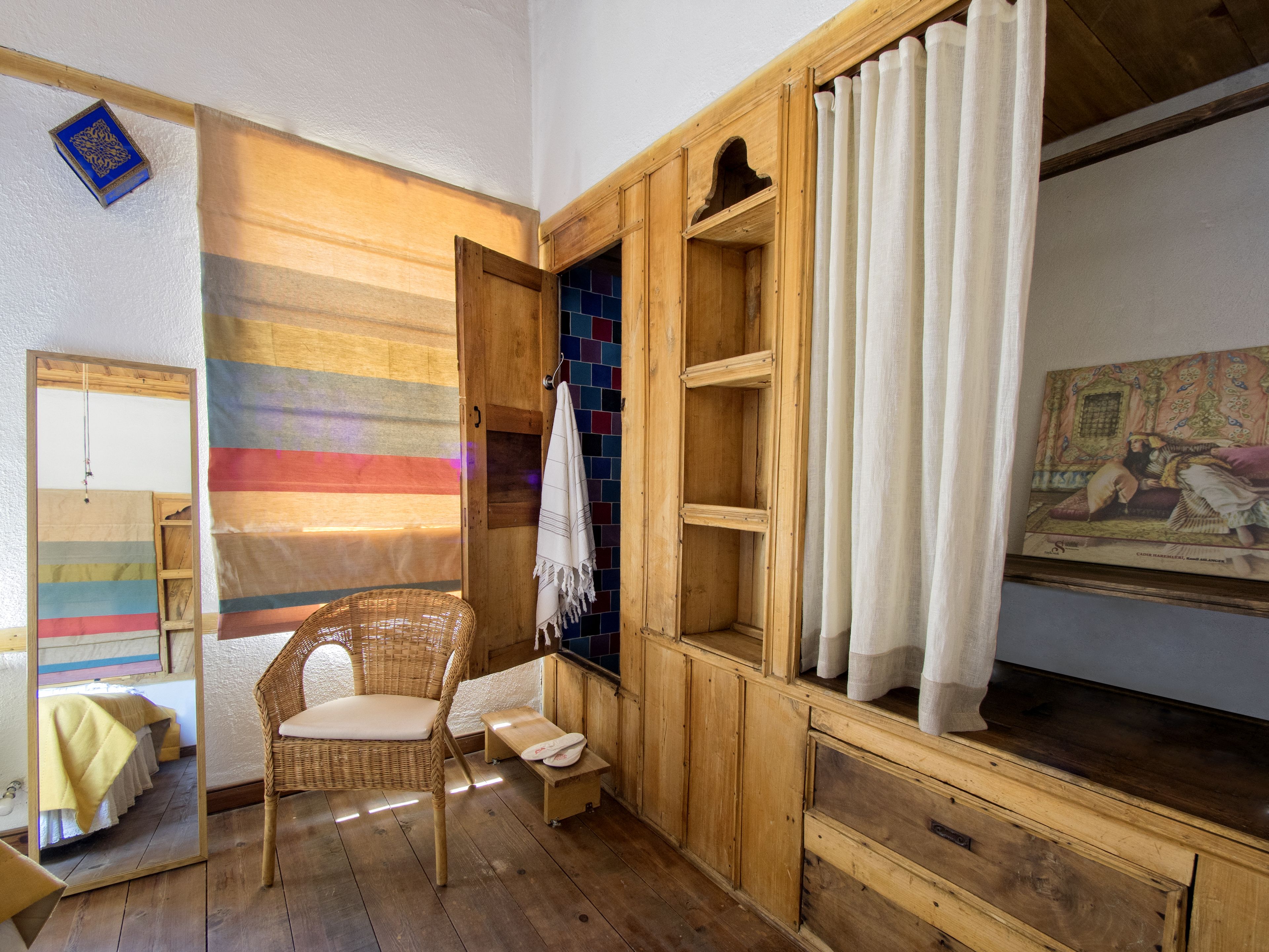 A room with a wooden cabinet, a wicker chair, a mirror, and a colorful striped wall.