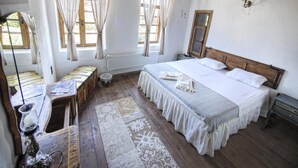 Ein Schlafzimmer mit einem hölzernen Bett, einem Nachttisch, einem Spiegel, einem Heizkörper und einem Fenster mit Vorhängen.