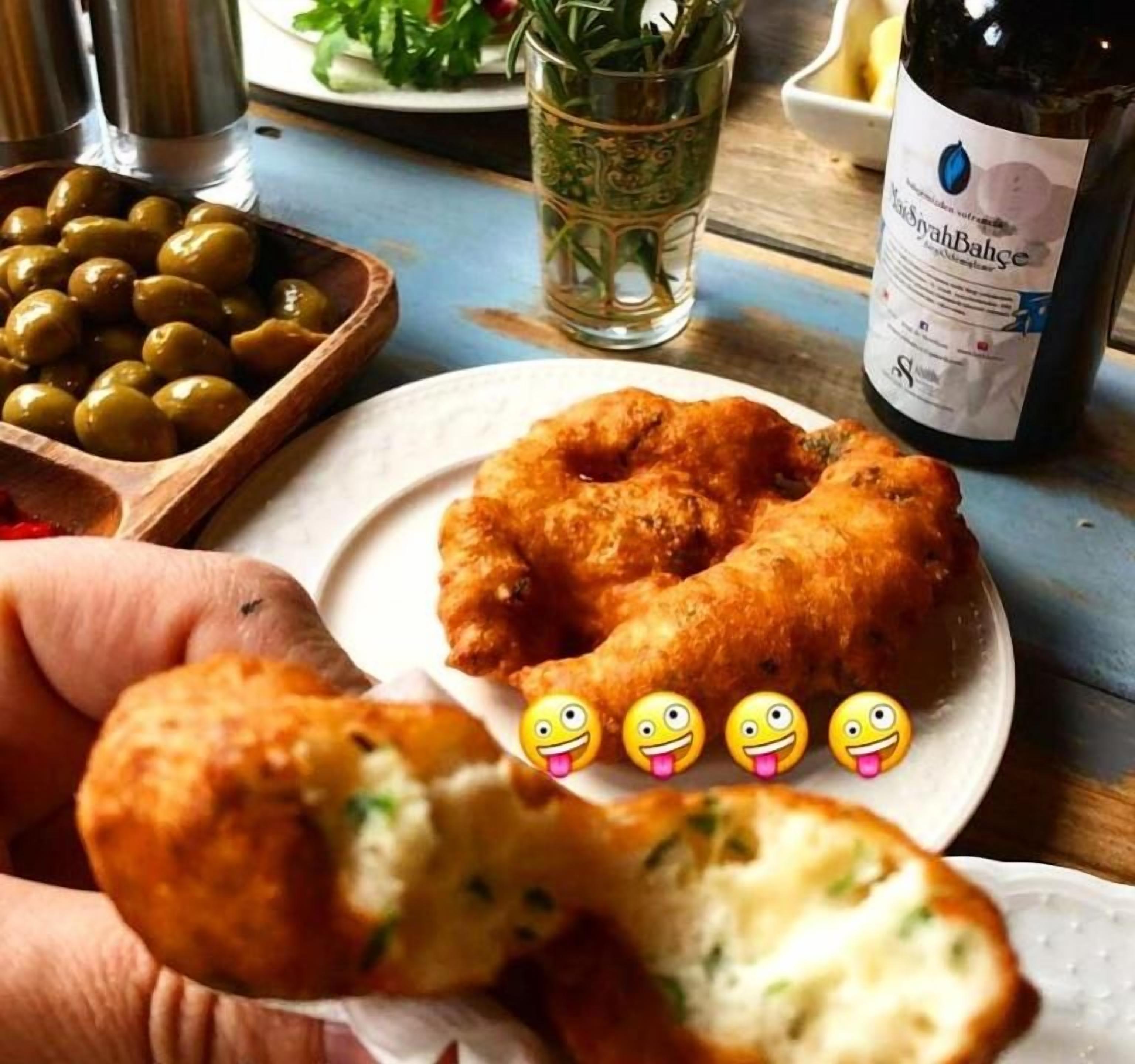 Un plato de comida frita, con una botella de vino y aceitunas al fondo.
