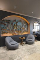 Un interior moderno con un mural grande, dos sillones grises, una mesita redonda y una lámpara.