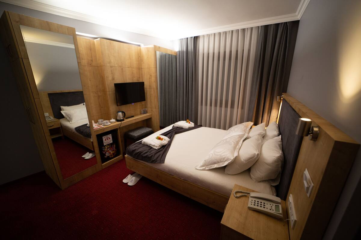 A hotel room with a large bed, a desk with a flat-screen TV, a mirror, and a telephone.