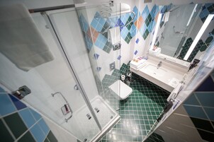 Un baño con cabina de ducha de vidrio, un lavabo blanco y piso de baldosas verdes.