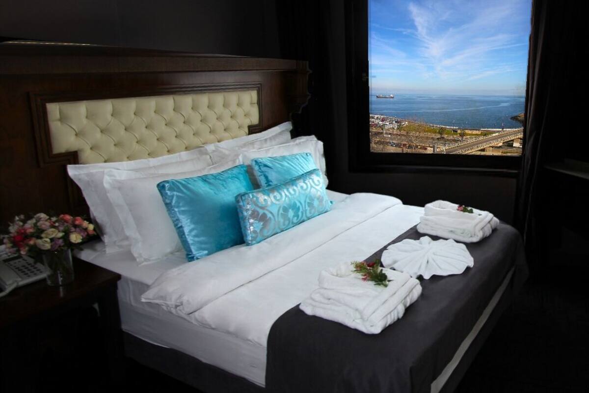 A hotel room with a large bed, a view of the sea, and a window with curtains.