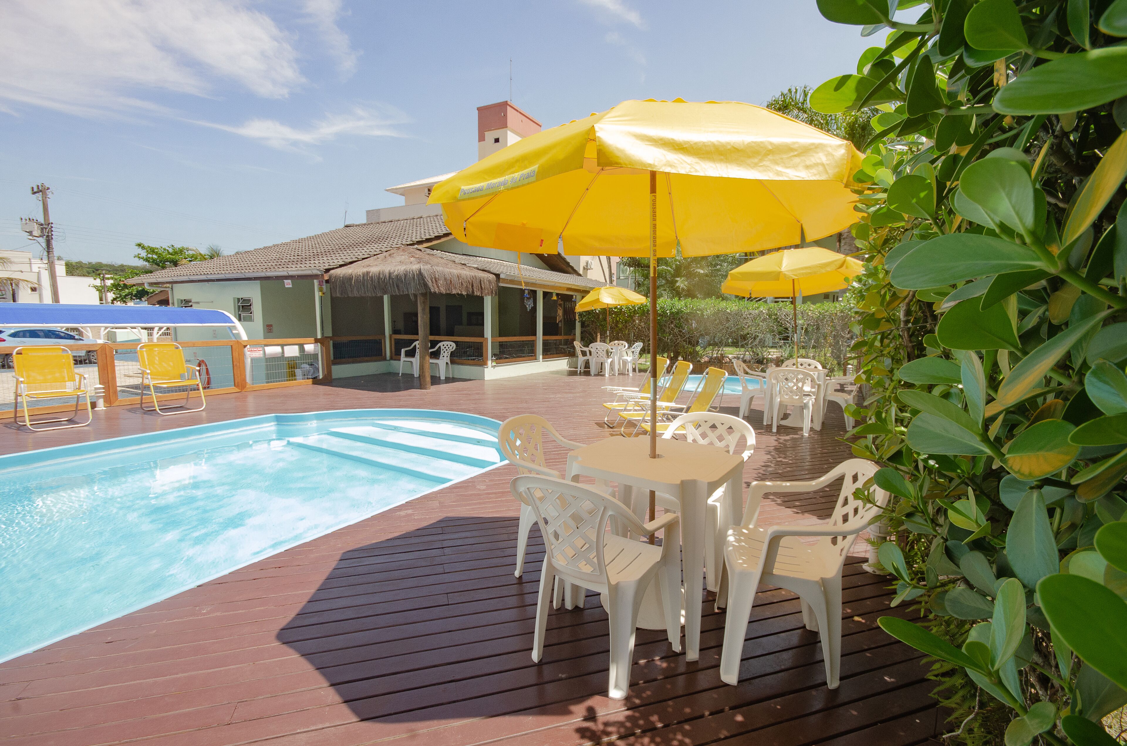 Een zwembadgedeelte met een houten terras, witte plastic stoelen en gele parasols.
