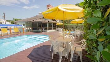 Una zona junto a la piscina con un deck de madera, sillas de plástico blanco y sombrillas amarillas.