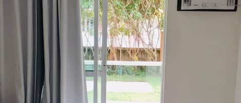 Habitación de hotel con cama, ventana con cortinas, unidad de aire acondicionado y vista a zonas verdes.