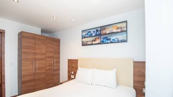 A modern hotel room with a large bed, wooden wardrobe, and a cityscape painting on the wall.