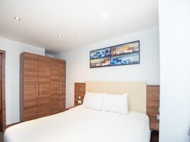 Un moderno cuarto de hotel con una cama grande, un armario de madera y una pintura de un paisaje urbano en la pared.