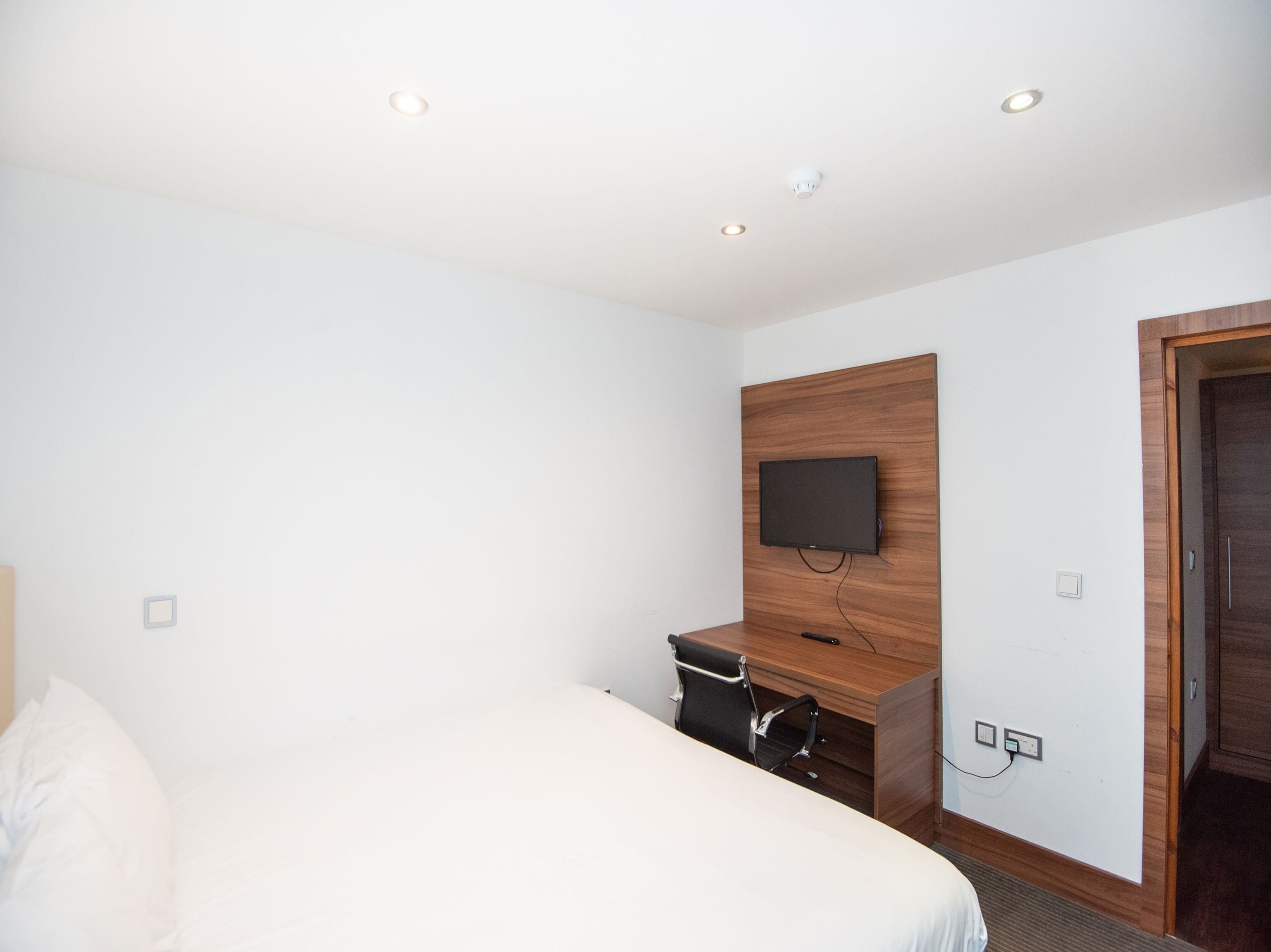 A hotel room with a bed, a desk, a television mounted on the wall, and a door.