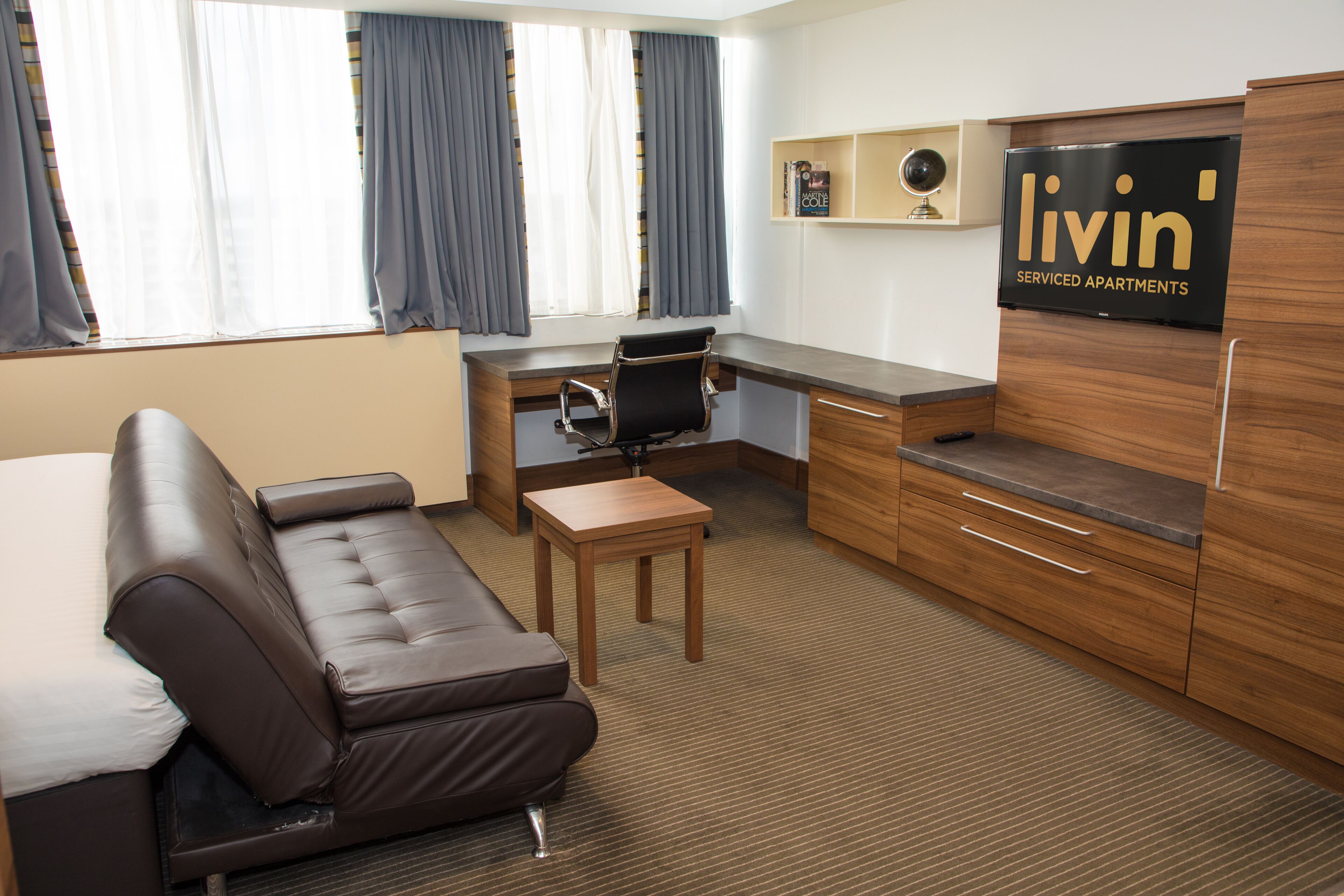 A hotel room with a sofa, desk, chair, TV, and a small table.