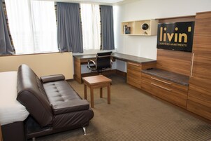 Habitación de hotel con sofá, escritorio, silla, televisión y una mesita.