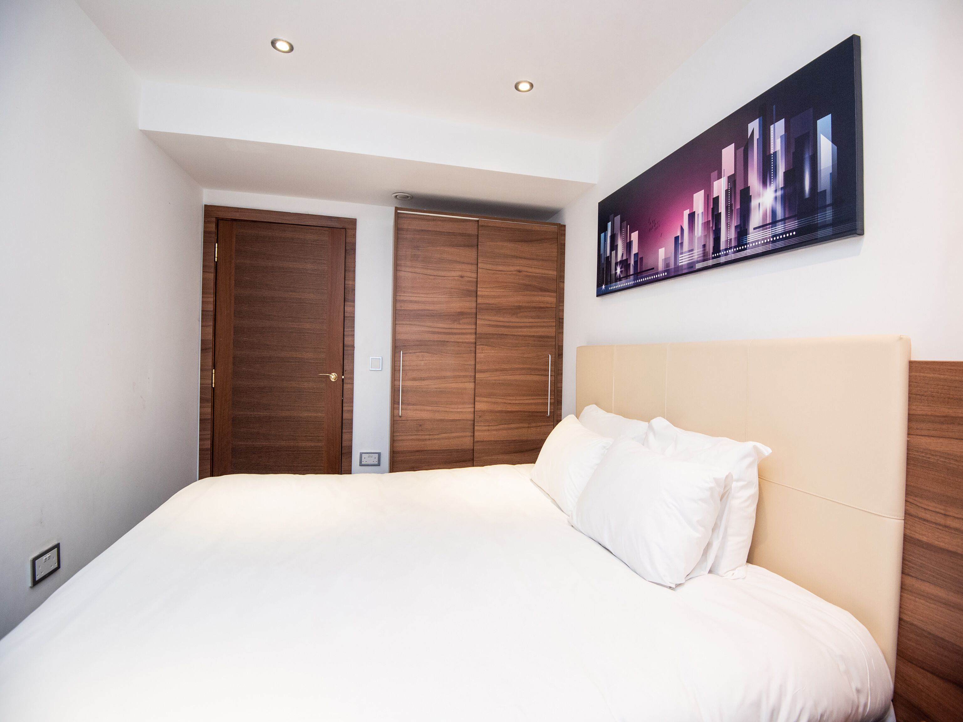 Un dormitorio con una cama grande, un armario de madera y un cuadro de un paisaje urbano en la pared.