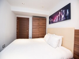 Un dormitorio con una cama grande, un armario de madera y un cuadro de un paisaje urbano en la pared.