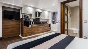A modern hotel room with a large bed, a built-in TV, a kitchenette, and a shower area. - Livin’ Serviced Apartments (Watford)