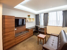 Una habitación de hotel moderna con un armario de madera, un televisor de pantalla plana, un escritorio con una silla, un sofá y una ventana con cortinas.