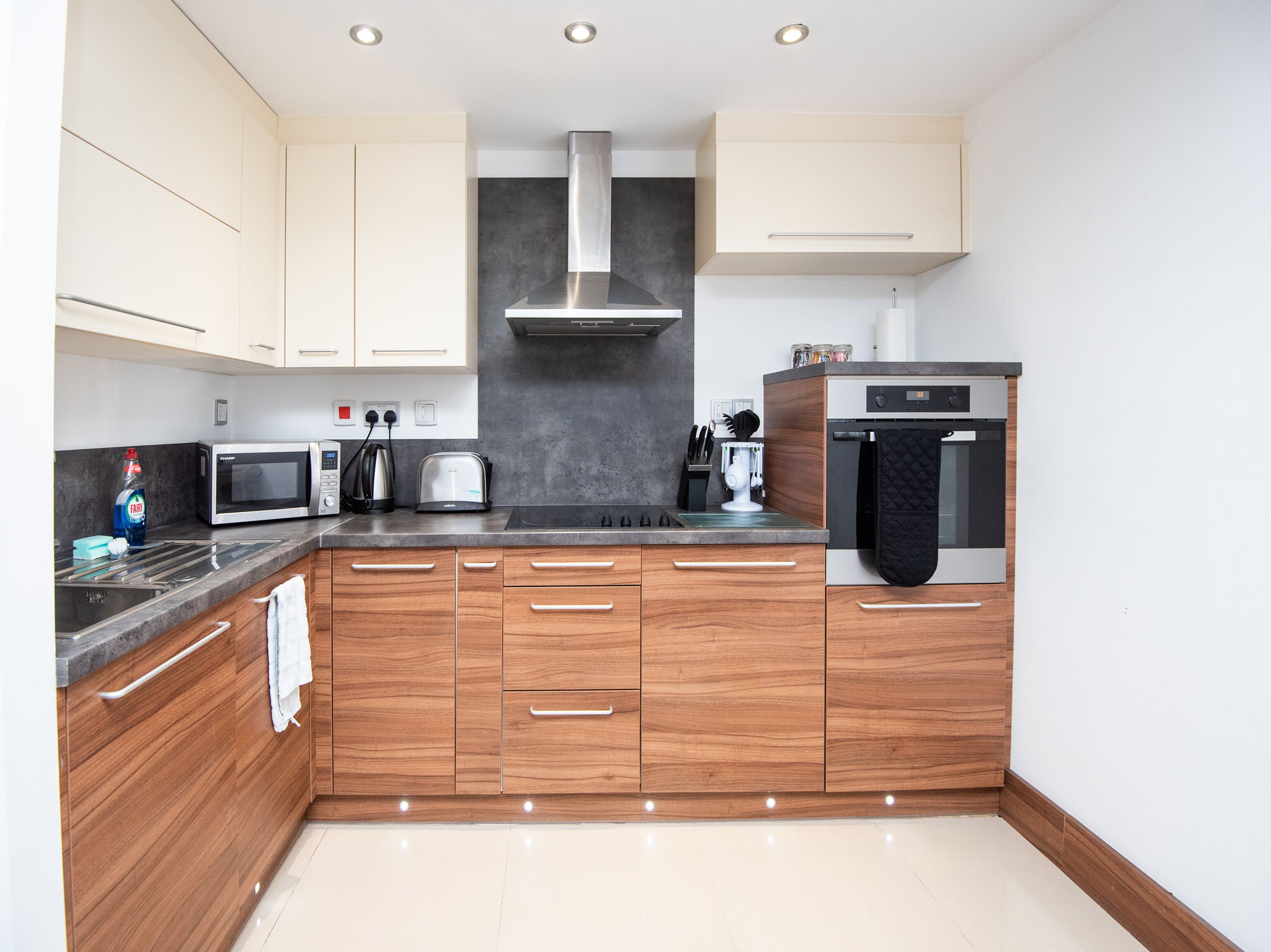 A modern kitchen with wooden cabinets, a stainless steel range hood, a microwave, a toaster, and an oven.