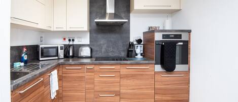 A modern kitchen with wooden cabinets, a stainless steel range hood, a microwave, a toaster, and an oven.