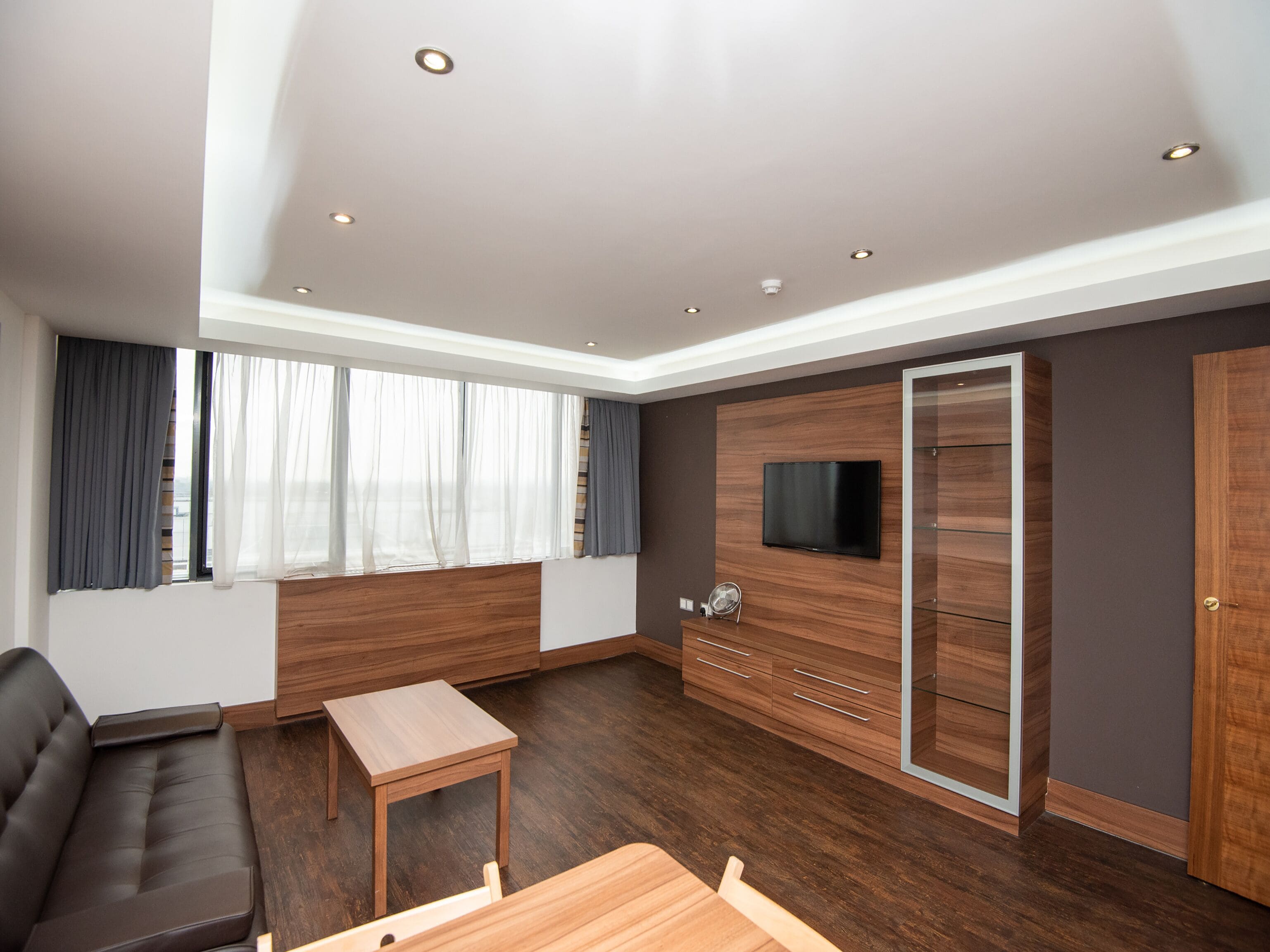 A modern living room with a sofa, a small table, a TV mounted on a wooden wall, and a sliding door closet.