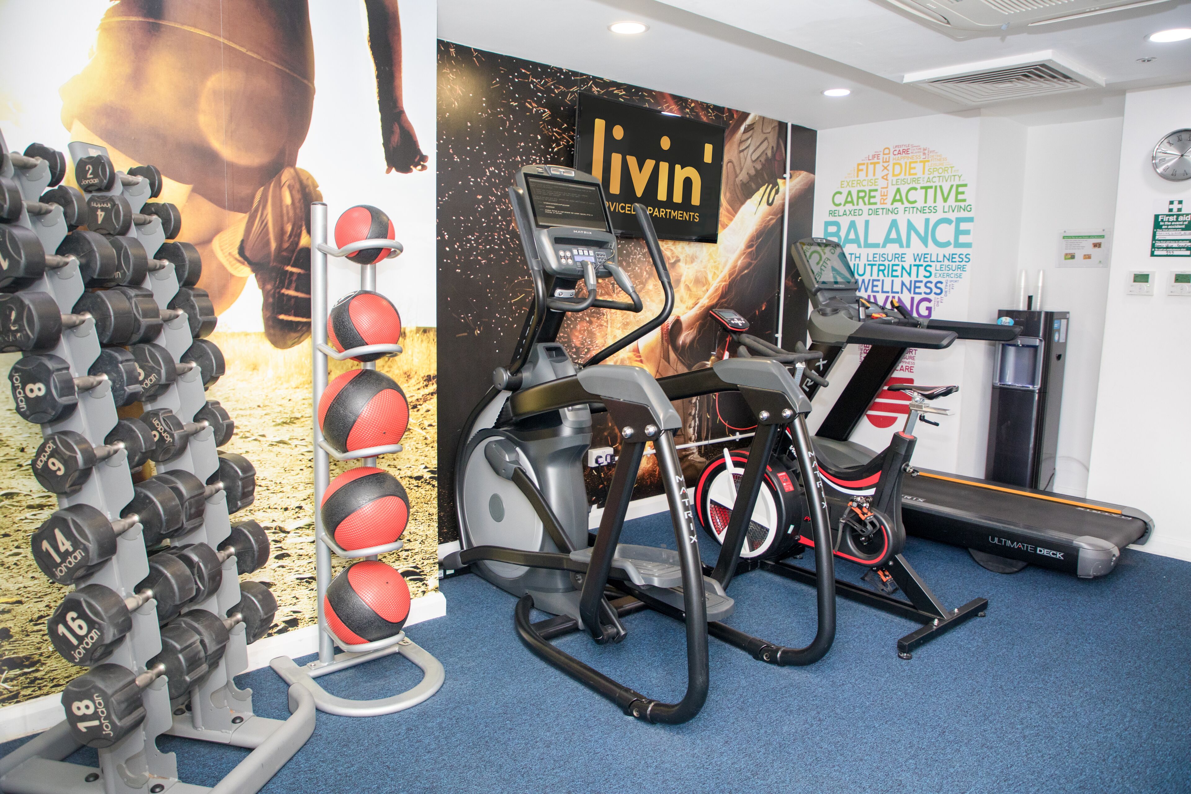 Een sportschool met trainingsapparatuur, een muur met motiverende woorden en een loopband.