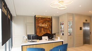 A modern kitchen with a central island, two blue chairs, a stainless steel refrigerator, and a decorative wall piece. - Livin’ Serviced Apartments (Watford)