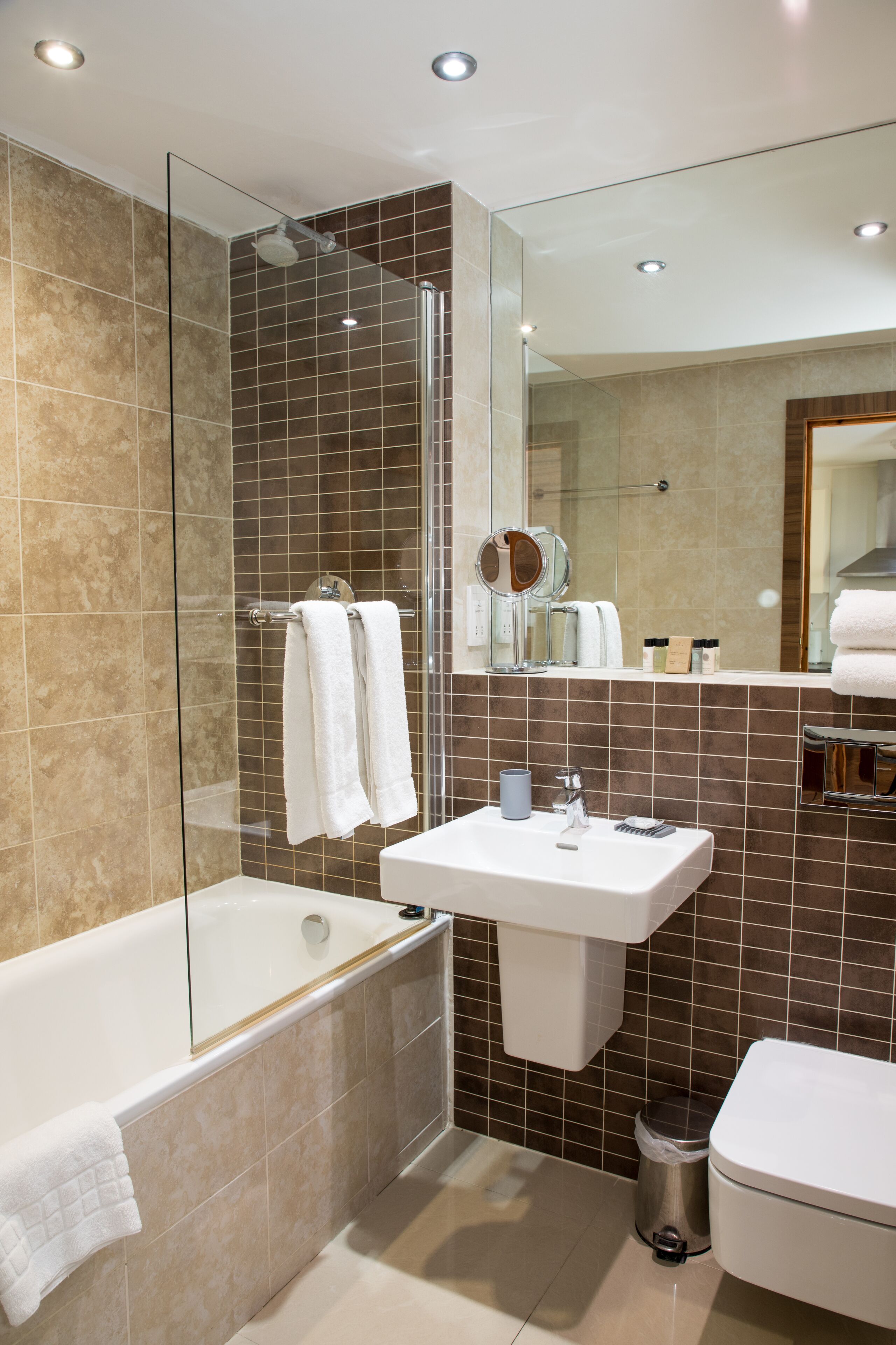 Ein modernes Badezimmer mit einer Duschkabine, einer weißen Badewanne, einem Waschbecken inklusive Spiegel und einer Toilette.
