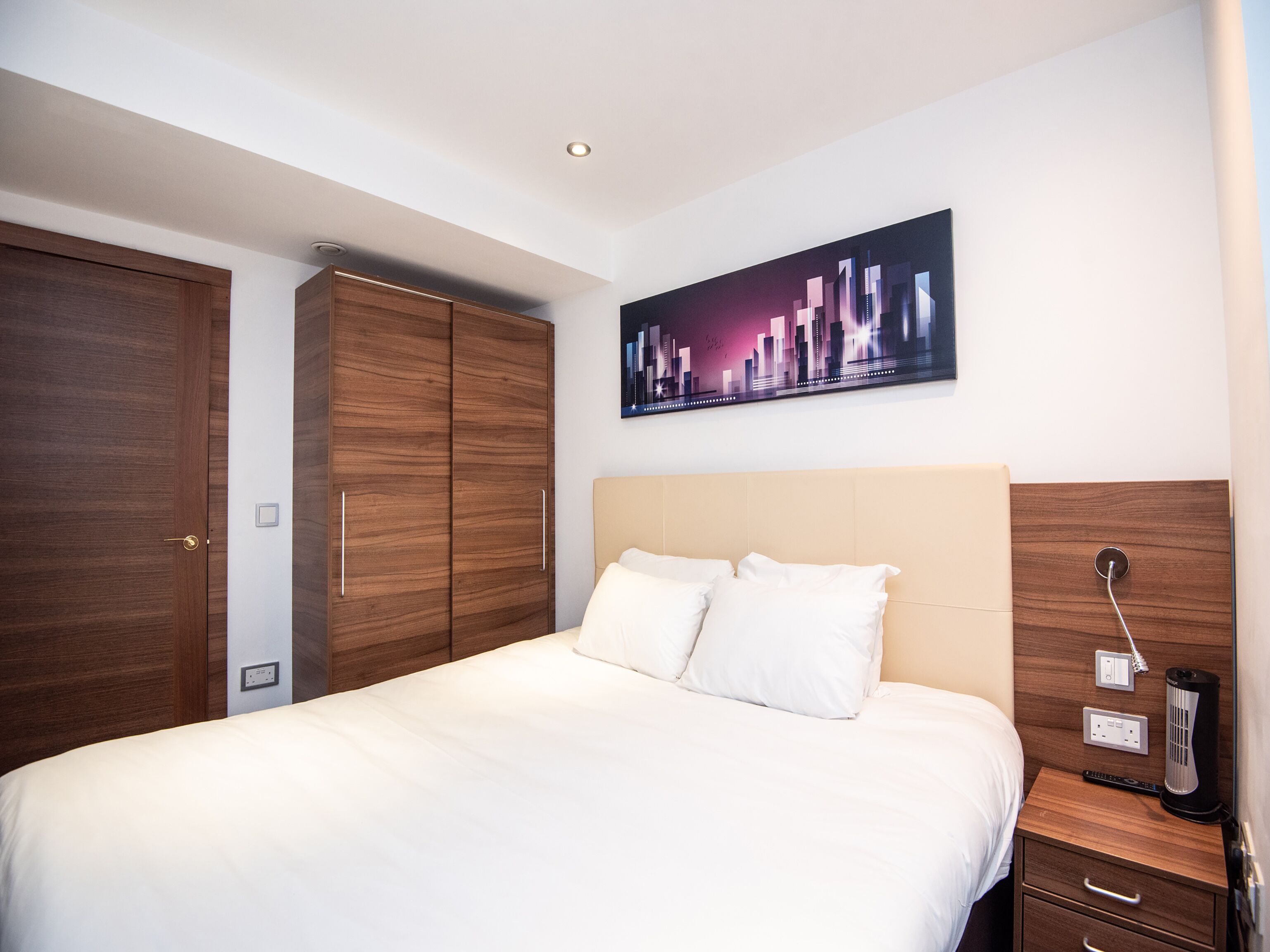 Habitació d'hotel amb un llit gran, un armari de fusta i un quadre de paisatge urbà a la paret.