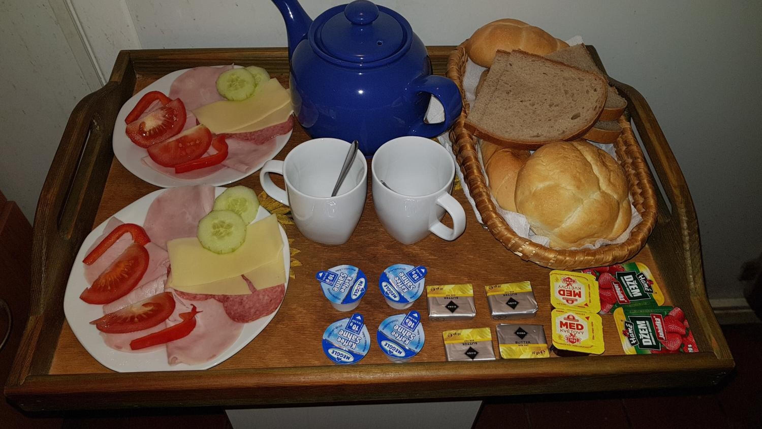 Una bandeja con alimentos, entre ellos, tomates en rodajas, pepinos, queso, pan y porciones de mantequilla.