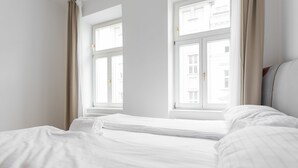 Habitación de hotel con dos camas, ventanas amplias y vistas a edificios.