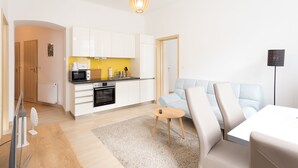 Una sala de estar moderna con un sofá, una mesa de centro y una zona de cocina con armarios blancos y un microondas.