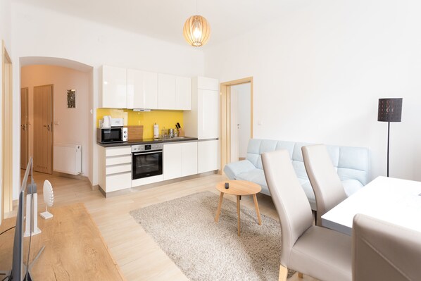 A modern living room with a sofa, a coffee table, and a kitchen area with white cabinets and a microwave.
