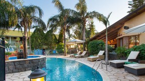 A swimming pool with lounge chairs and umbrellas, surrounded by palm trees and stone flooring. - Out of Africa Sea of Galilee Resort (Had Nes)