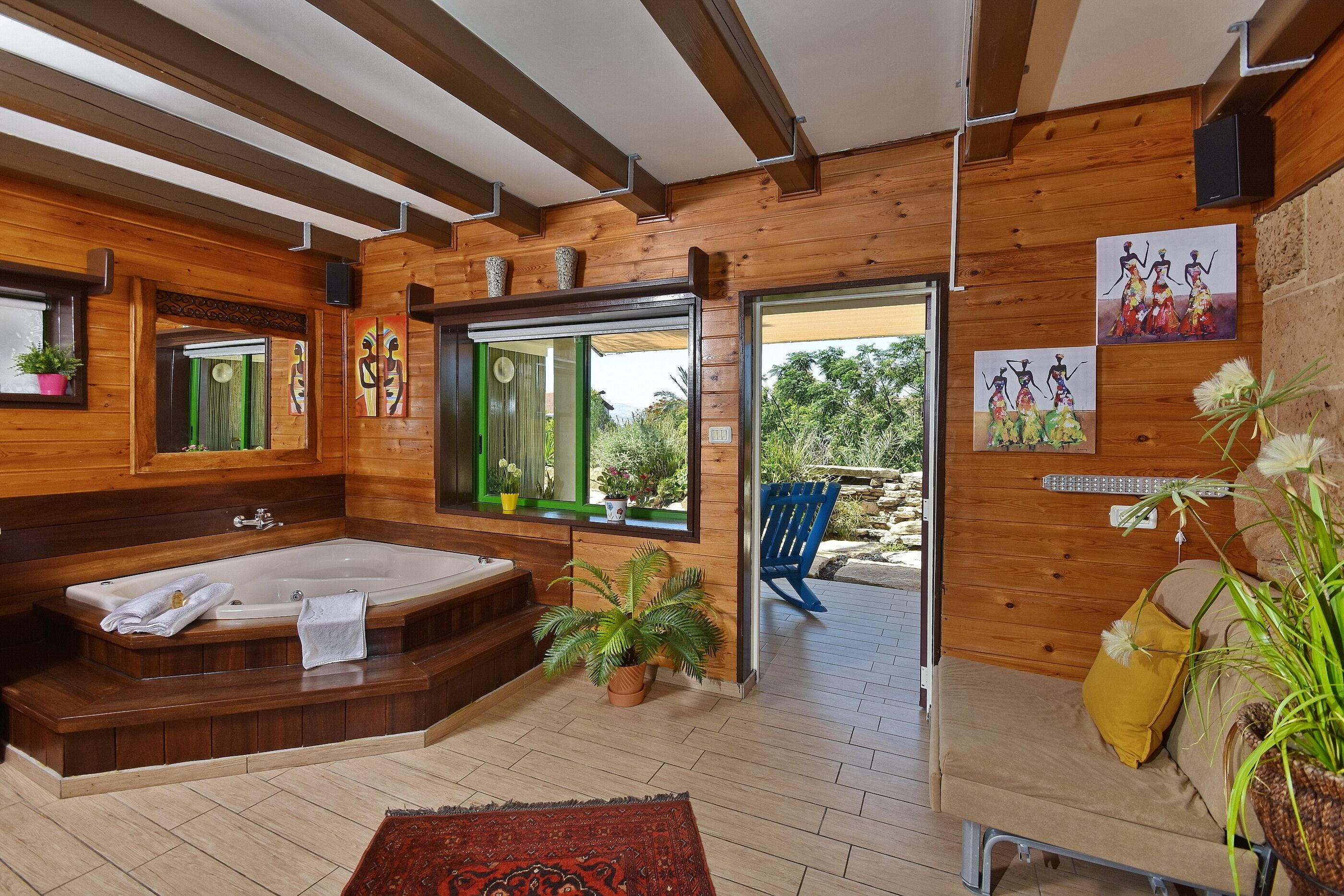 A wooden cabin with a large bathtub, a sofa, and a window with a view of greenery.