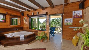 A wooden cabin with a large bathtub, a sofa, and a window with a view of greenery.