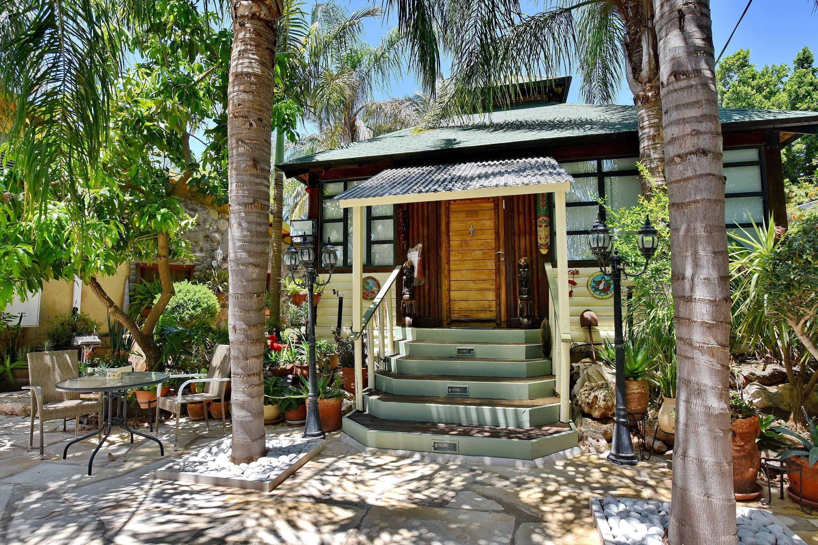 A tropical-style building with a wooden front door, a porch with chairs, and a staircase leading to the entrance.