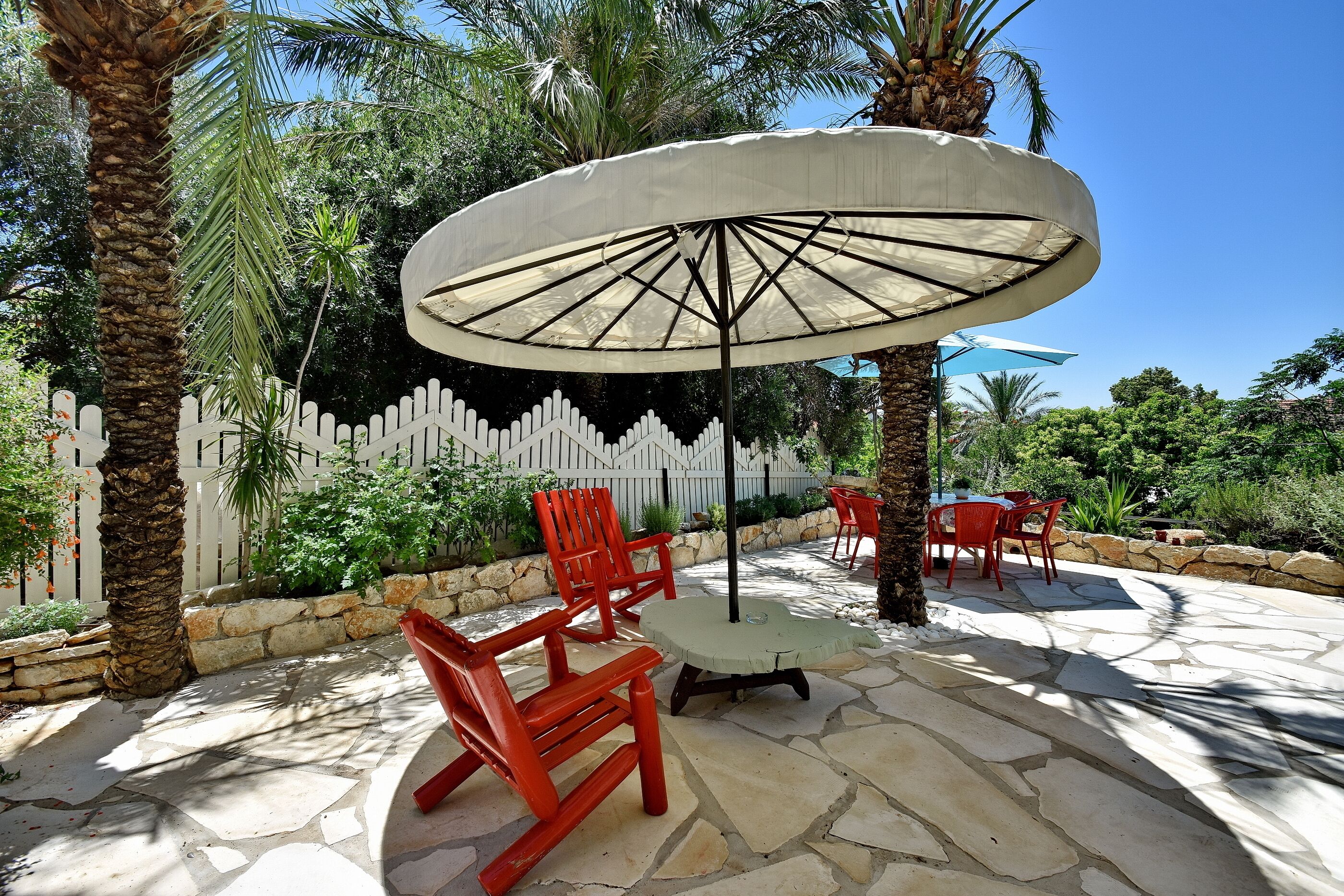 An outdoor patio with stone flooring, red chairs, a table, and a large umbrella.