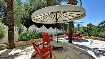 An outdoor patio with stone flooring, red chairs, a table, and a large umbrella.