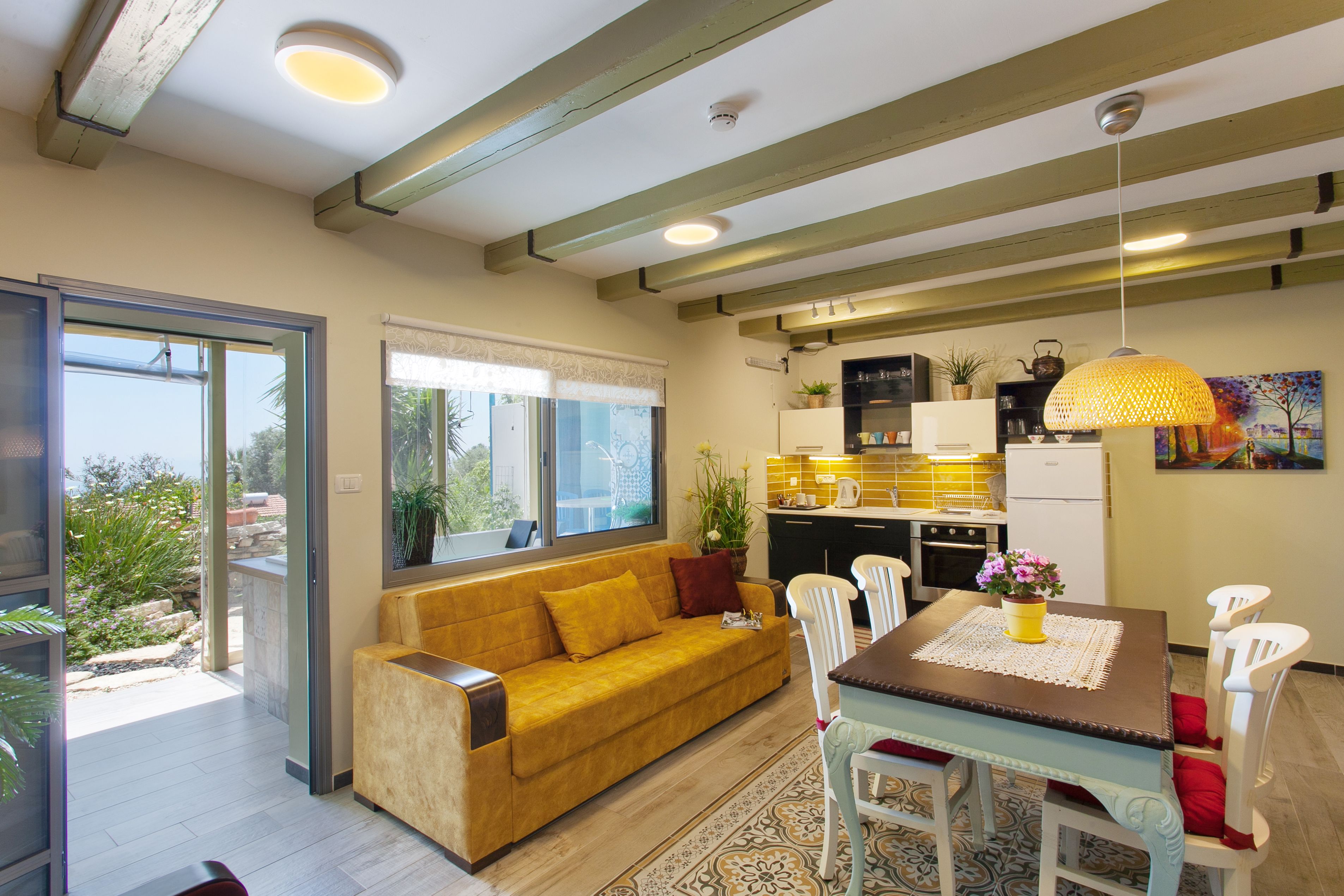 A modern kitchen with a dining area, a sofa, and a view of the outdoors.