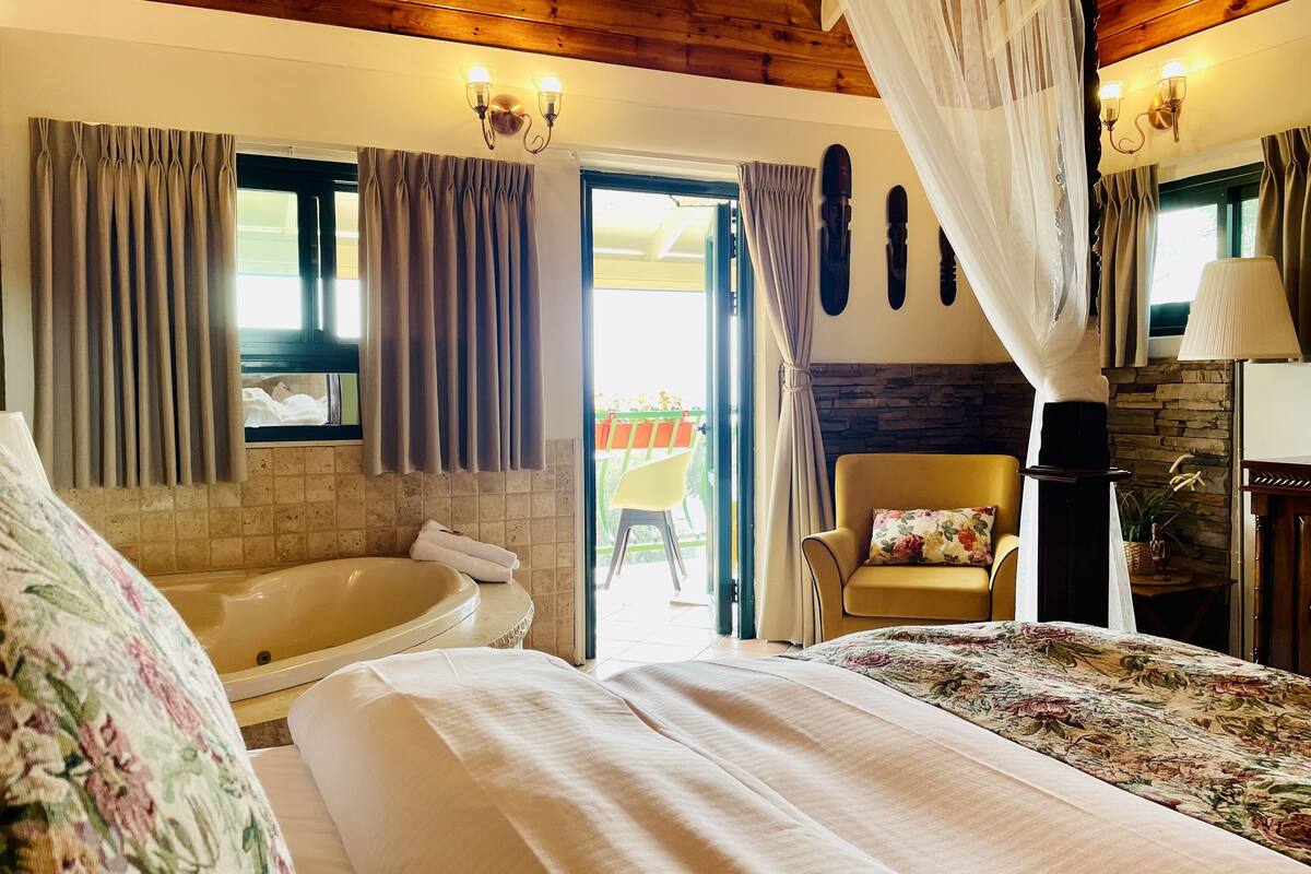 A bedroom with a large bed, a bathtub, and a chair.