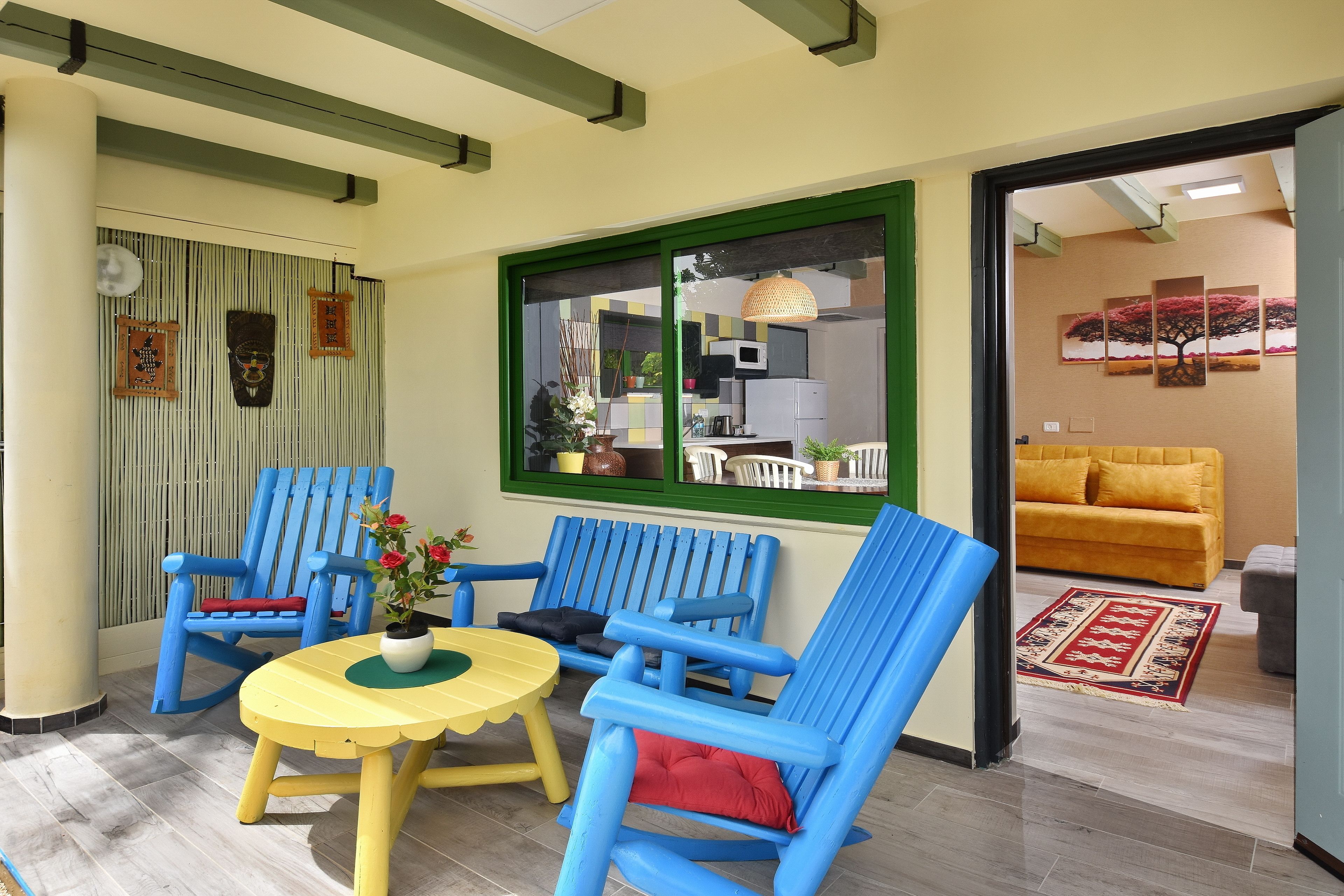 Una habitación con ventana de marco verde, una mesa amarilla, sillas azules y un sofá amarillo.