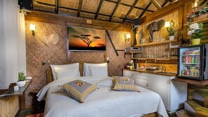 A room with a bed, a nightstand, a shelf with decorative items, and a refrigerator. - Out of Africa Sea of Galilee Resort (Had Nes)