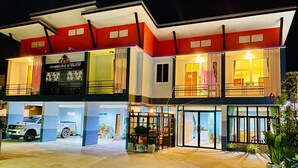 A two-story building with a modern design, featuring a large entrance with glass doors and a parking area with a white SUV. - Graphic House at Chiang Rai (Chiang Rai)