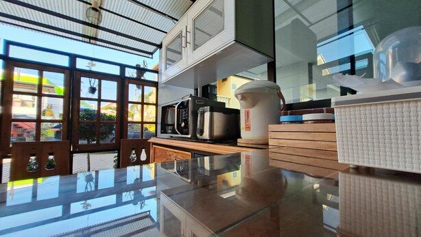 A modern kitchen with a glass-top countertop, stainless steel appliances, and a view of the outside through large windows. - Graphic House at Chiang Rai (Chiang Rai)