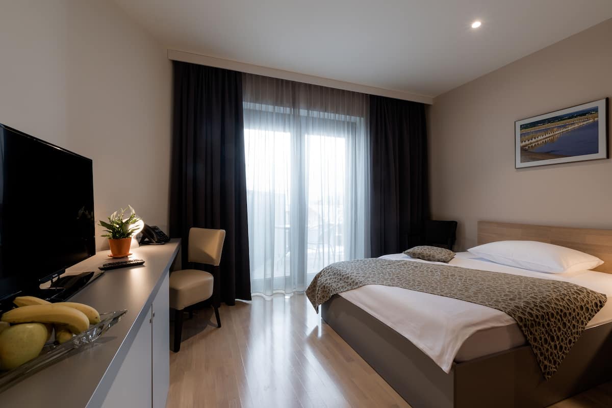 Una habitació d'hotel amb un llit, una taula de treball amb un televisor, una cadira i una finestra amb cortines.