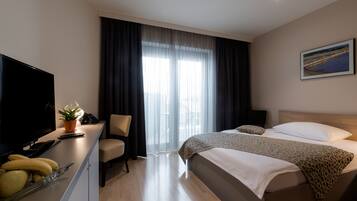 Habitación de hotel con cama, escritorio con televisor, silla y ventana con cortinas.