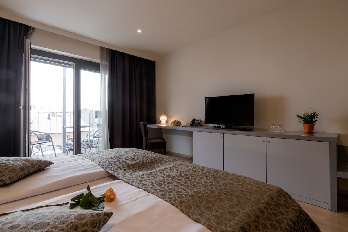Habitació d'hotel amb llit, escriptori amb televisor, planta en test i balcó amb cadires.