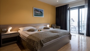 A modern hotel room with a large bed, a nightstand with a lamp, a painting on the wall, and a balcony with a view.